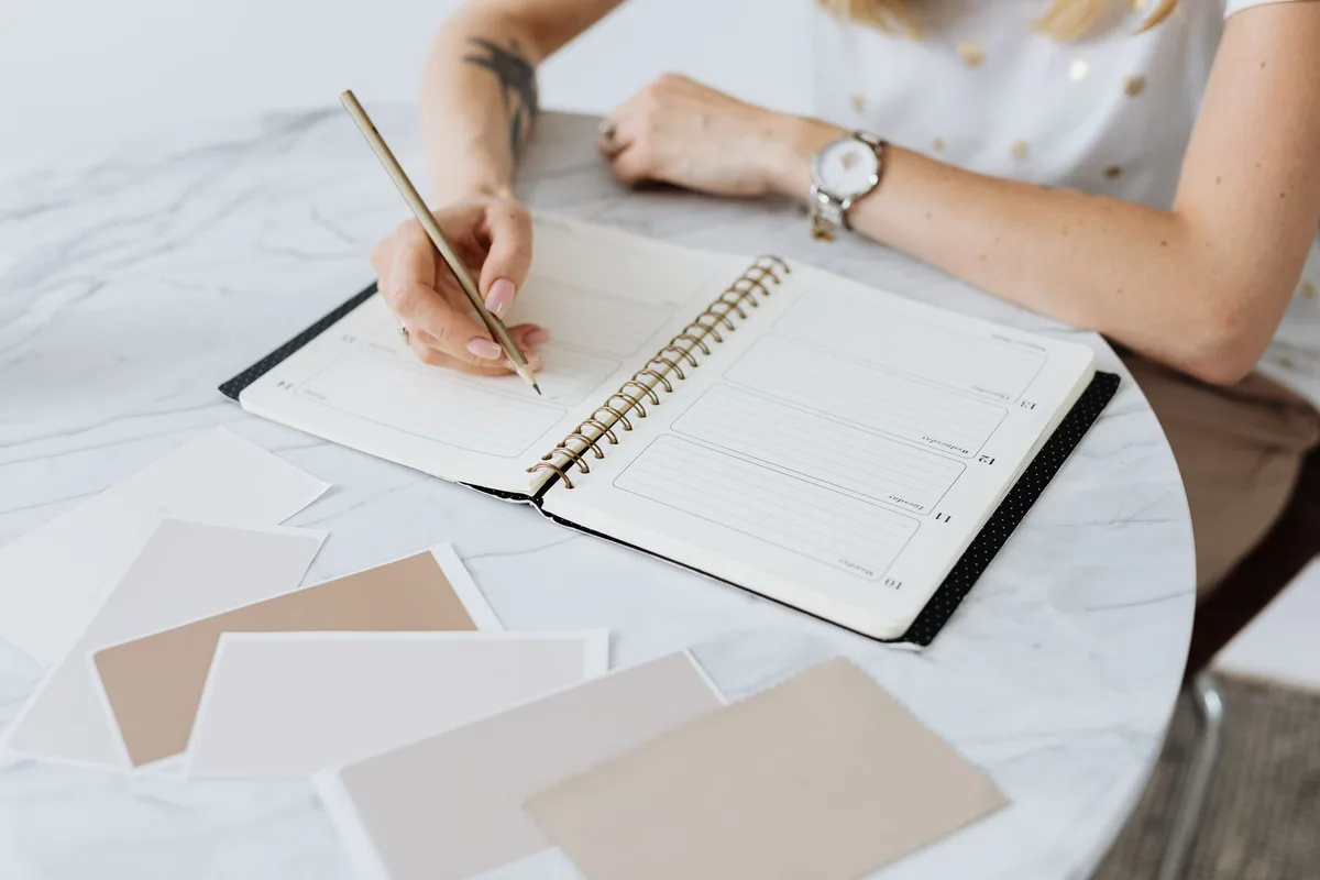 A person writing notes in a planner at a desk, working through options methodically rather than sketching from pure enthusiasm