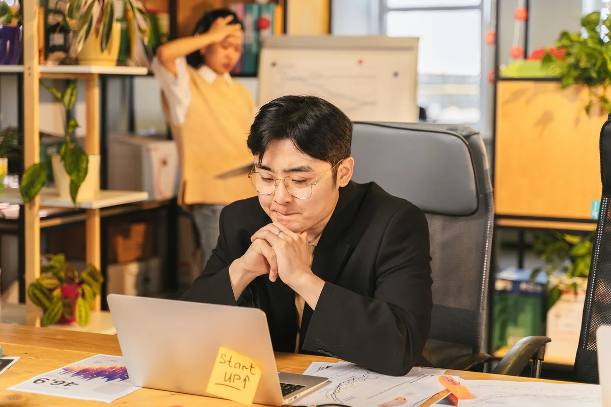A solo founder sitting at a desk with a laptop, hand on chin, looking thoughtful about whether to proceed with an idea
