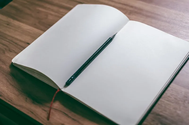 A notebook open on a desk with several idea concepts written down, one crossed out, a pencil lying alongside