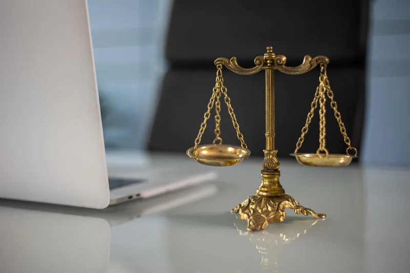 A golden balance scale beside a laptop, representing the cost-benefit analysis of stopping versus continuing